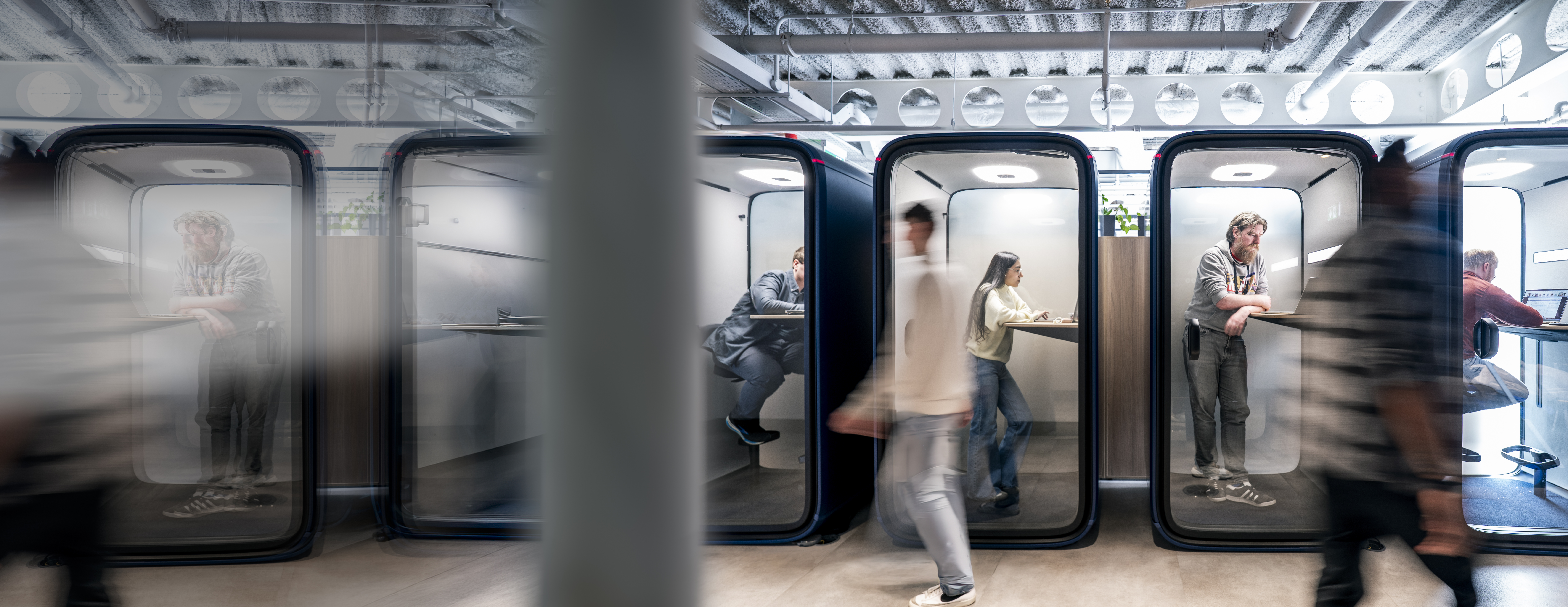 Employees working and moving through individual focus booths in a modern Liberty IT office.