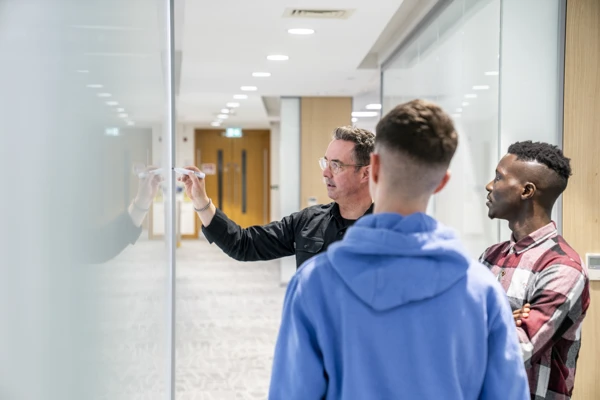 Employees discussing ideas at a whiteboard in a Liberty IT office hallway.