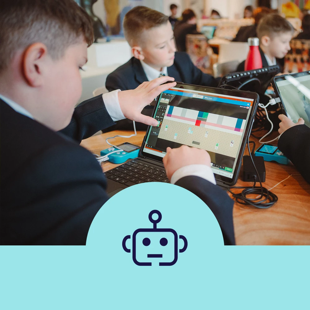 Children in a classroom setting are using computers and tablets for coding with a focus on Scratch. They're sitting at a wooden table, engaged with electronic devices.