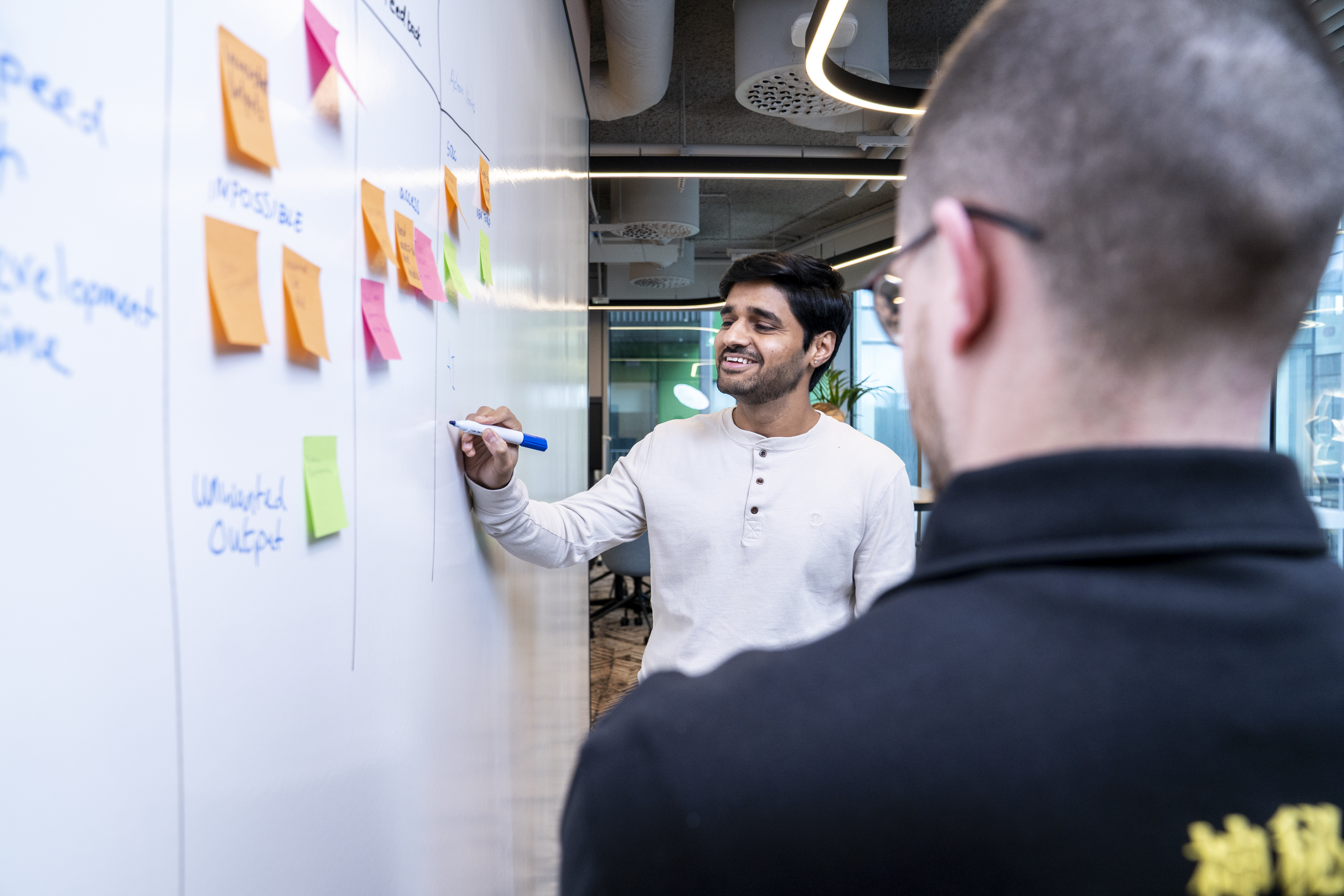 Employees collaborating at a whiteboard during a planning session in a Liberty IT office.